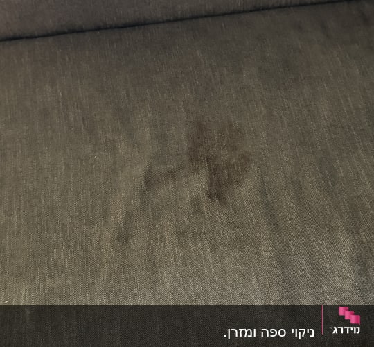 תקריב של כתם על ספת בד אפורה לפני ניקוי